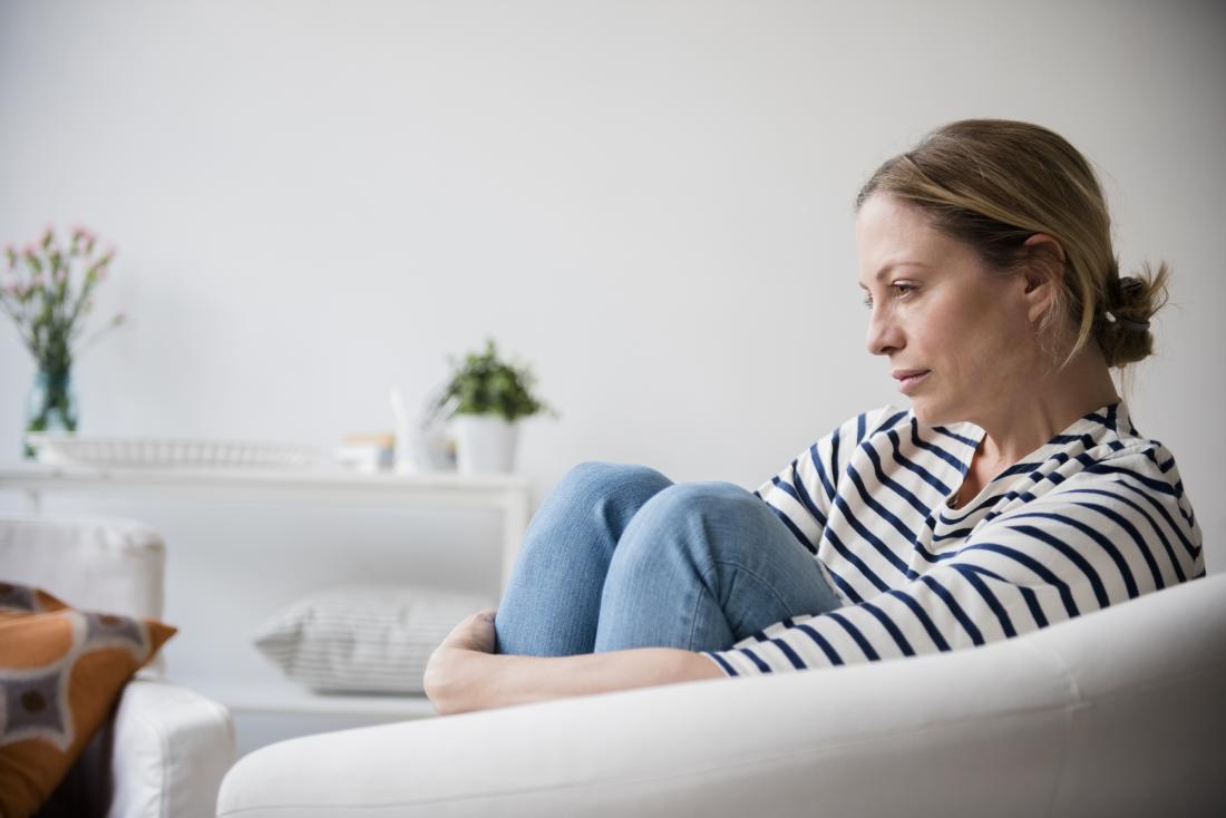 Sad and worried woman holding legs while sitting on armchair