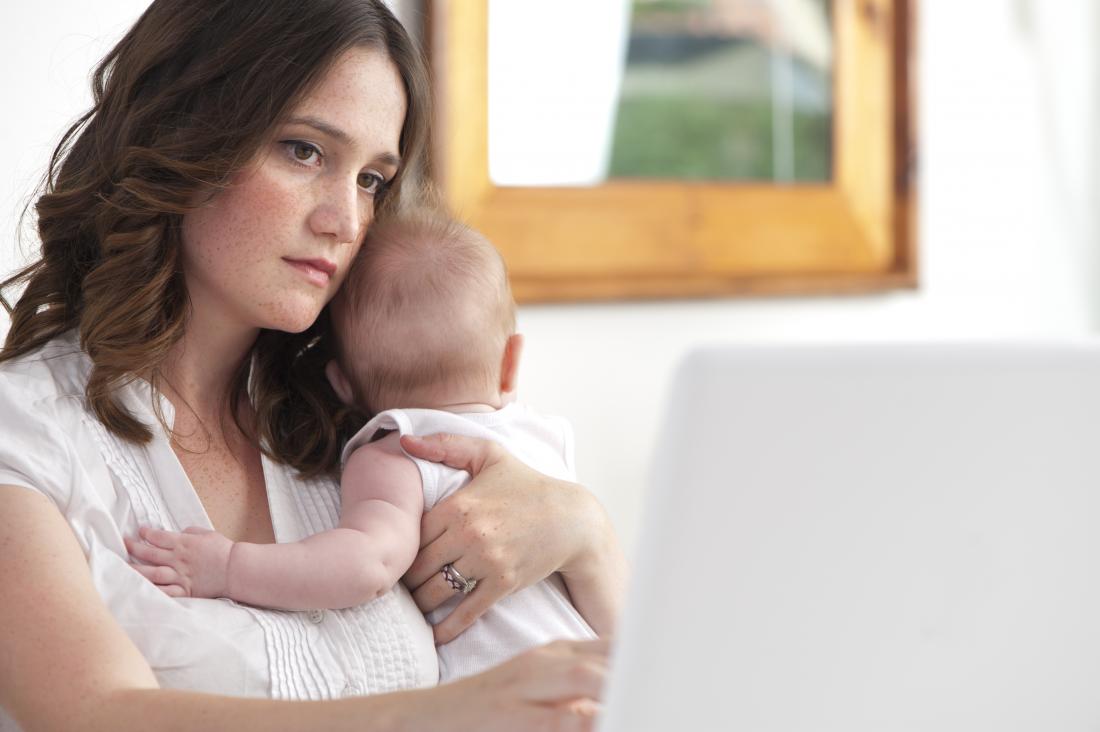Young mother holding baby while working from home.