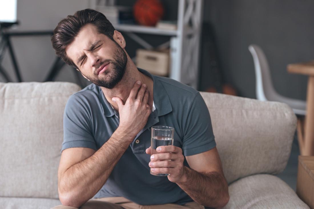 Man with sore throat having trouble swallowing, holding glass of water.