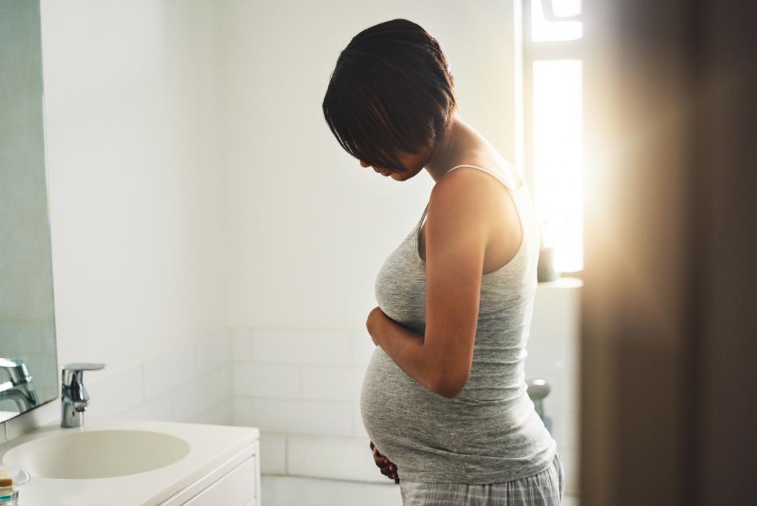 Pregnant woman in her bathroom holding her stomach