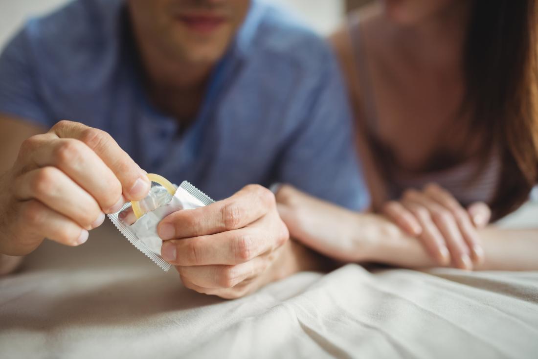 couple on bed with man removing condom from package