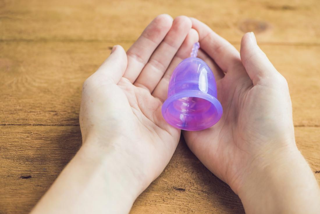 Woman holding purple menstrual cup over wooden table