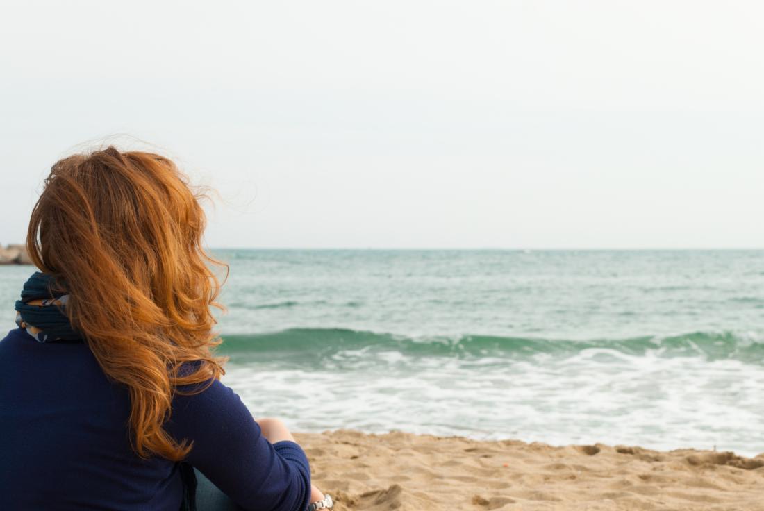 Woman with red hair sat on a beach