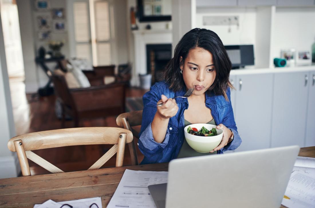 Woman eating a salad in front of her laptop