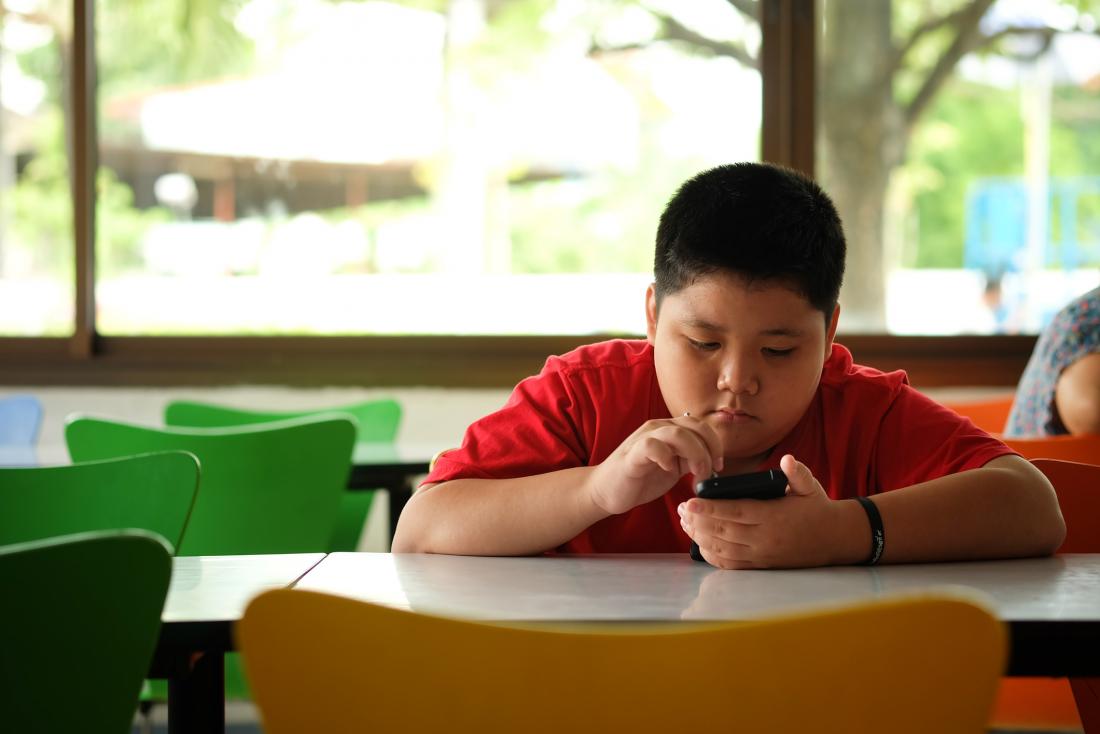 young boy with obesity looking sad sitting at a table