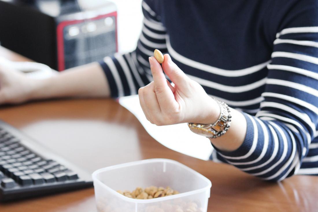 Woman at desk at work snacking and eating on peanut