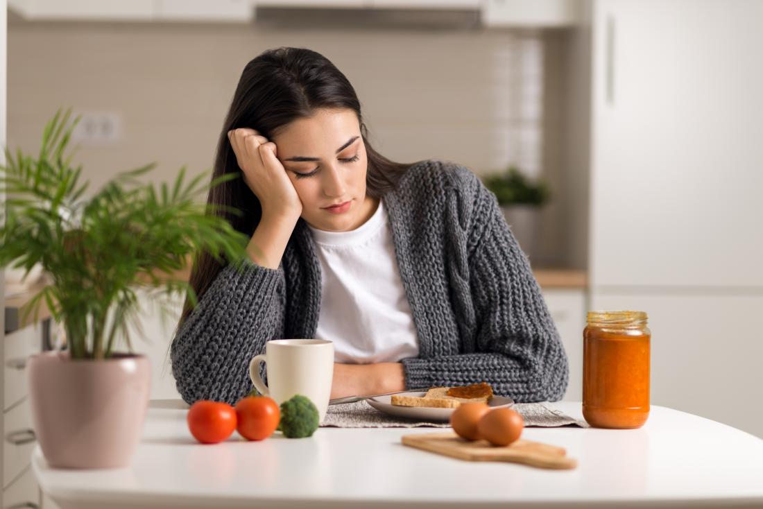 Woman looks at plate of food but can't eat due to heartburn and nausea.