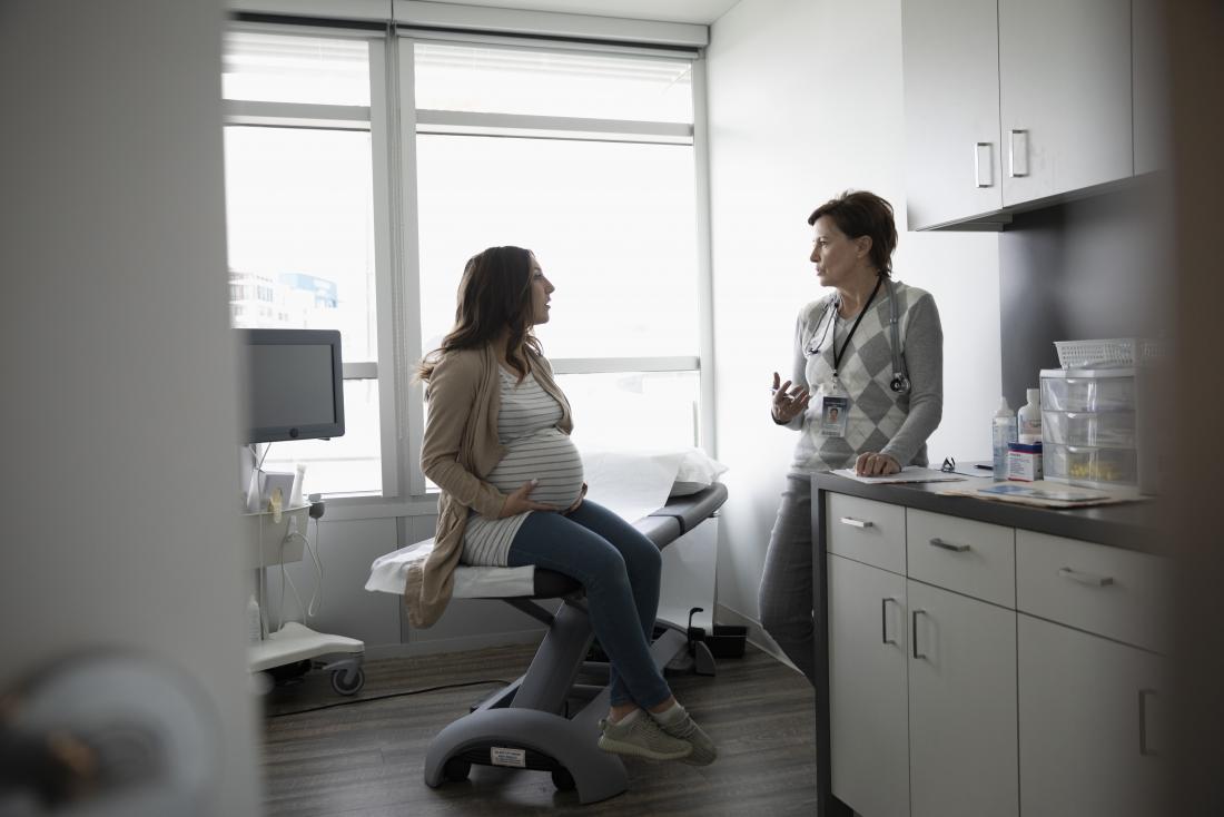 Pregnant woman with ulcerative colitis speaking to doctor, obstetrician, or gynecologist in office.
