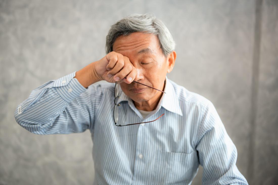 A senior man experiencing steroid side effects holds his glasses and rubs his eyes.