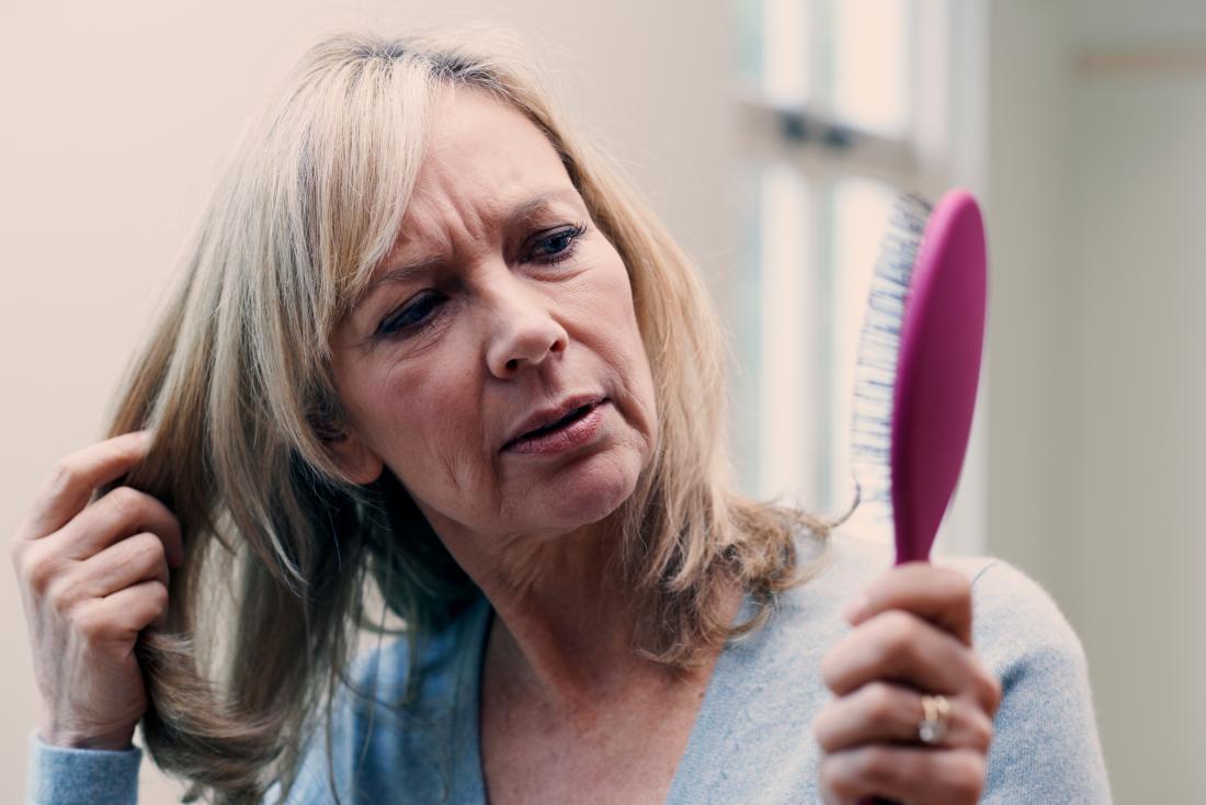 a woman looking at a hair brush and wondering if saw palmetto might help stop her hair from falling out