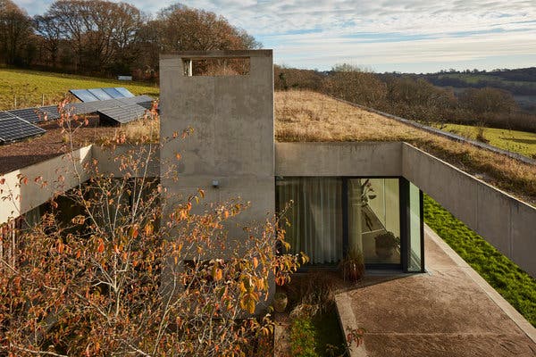 The green roof serves as an extension of the meadow above, providing natural insulation. A courtyard below overlooks the Wye Valley.