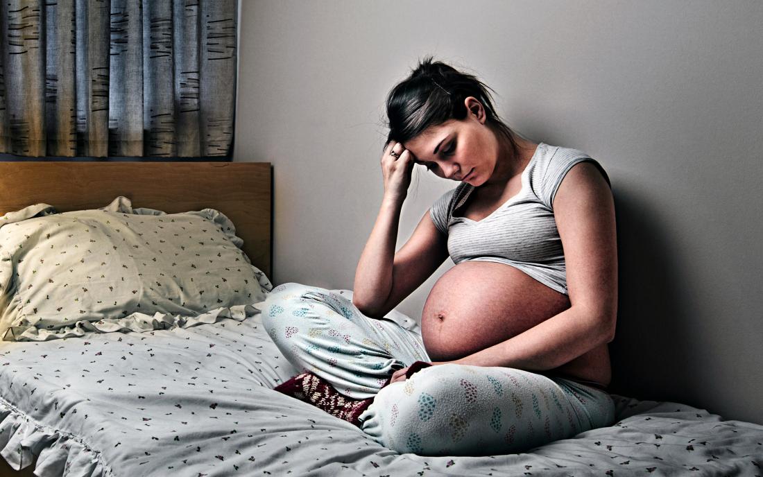 a woman sat on a bed and experiencing Depression during pregnancy