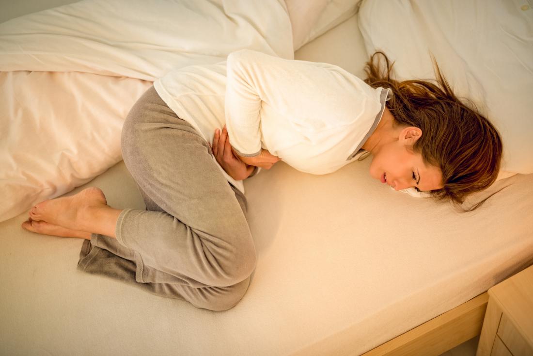 woman laying on bed with stomach cramps 