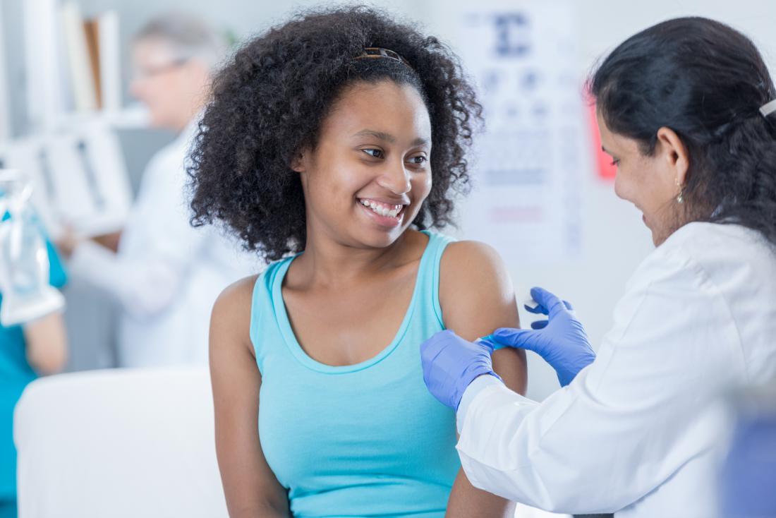 young woman receiving hpv vaccine having plaster put over injection site by nurse
