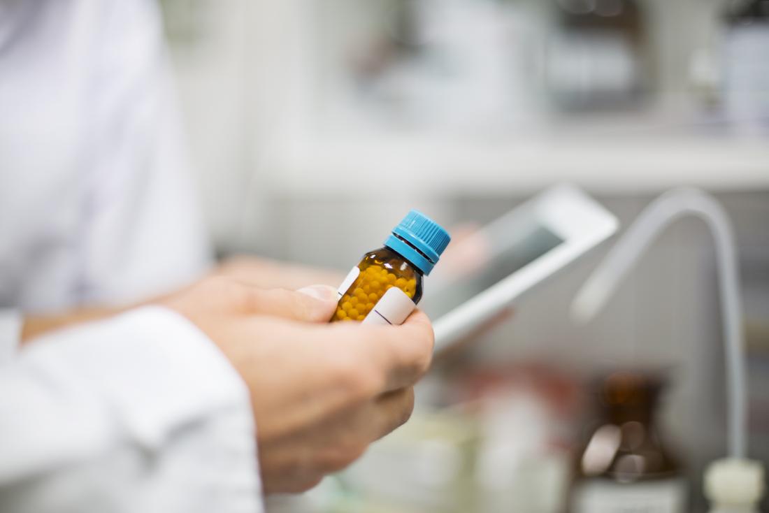 Researcher in lab coat holding bottle of pills and tablet