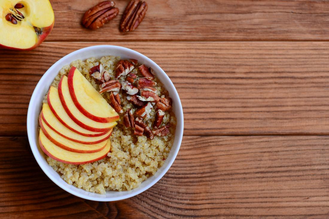 Quinoa porridge with fruits and nuts topping. Vegan quinoa porridge with apples and pecan nuts in a white bowl and on brown wooden background. Healthy breakfast.