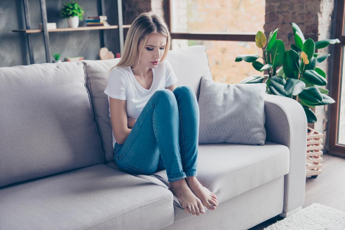 Woman with cramps holding stomach sitting on sofa
