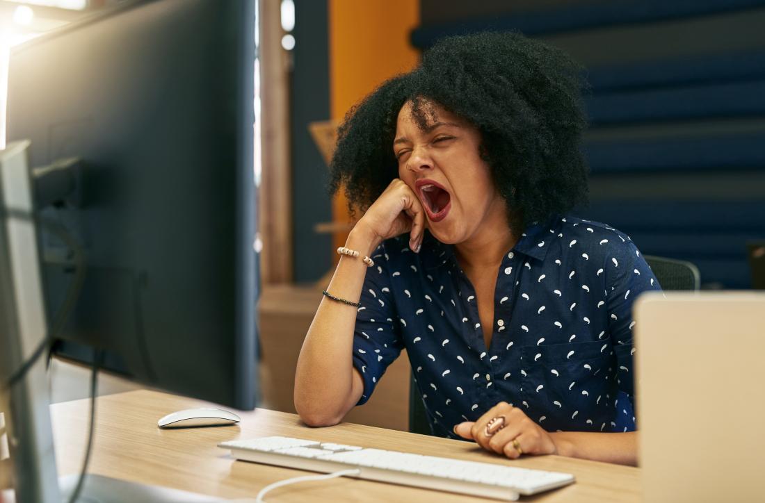 Tired woman in office yawning at desk after eating