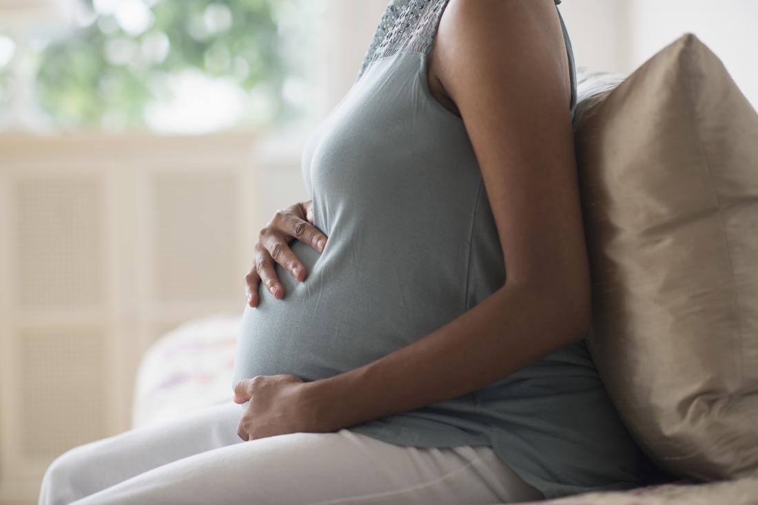 pregnant woman sitting side profile holding baby bump