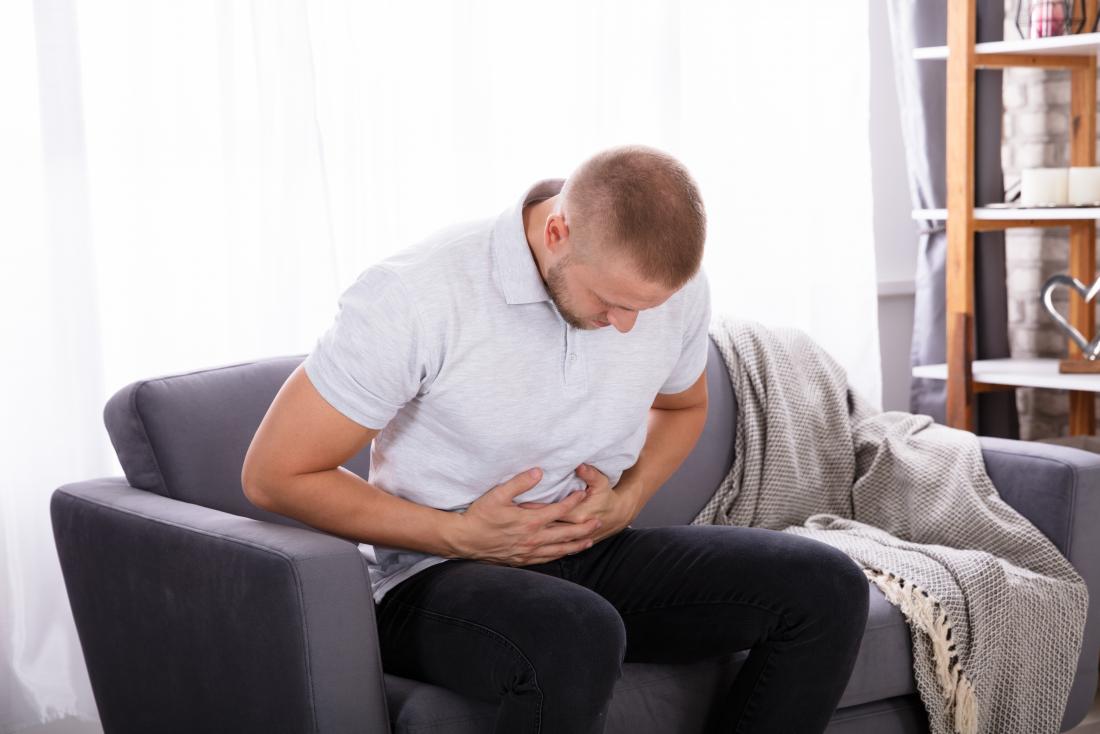 man sitting on sofa holding his stomach in pain