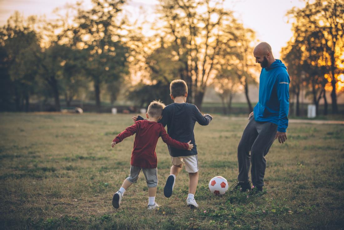 Kids playing football with their dad in a park
