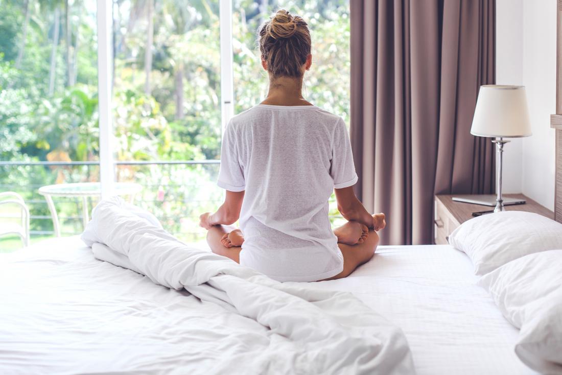 Woman sat on her bed meditating which may help with irregular periods