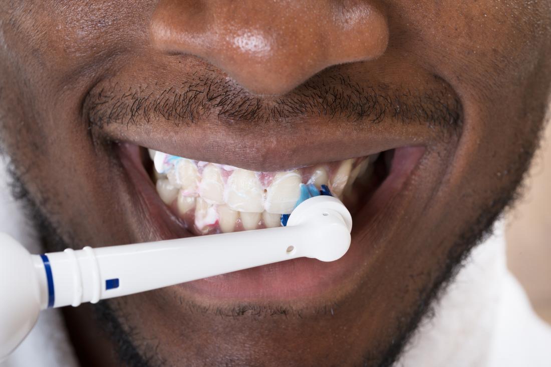 close up of man cleaning teeth with electric toothbrush