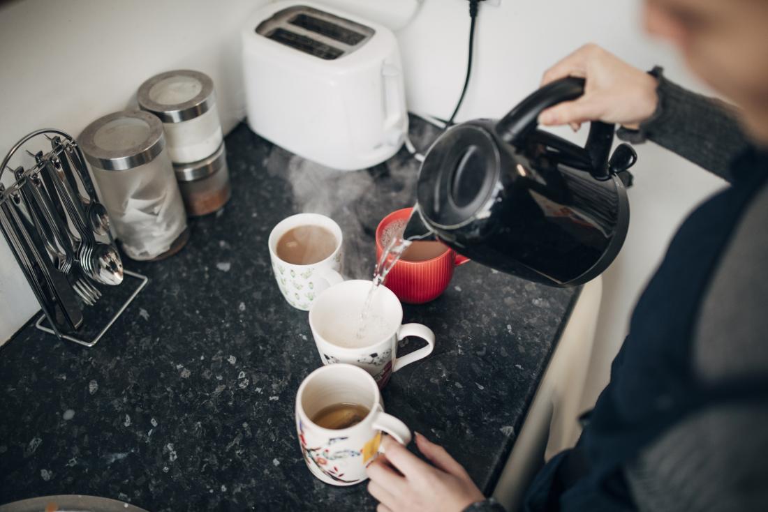 Person making coffee and tea hot drinks in a kitchen.