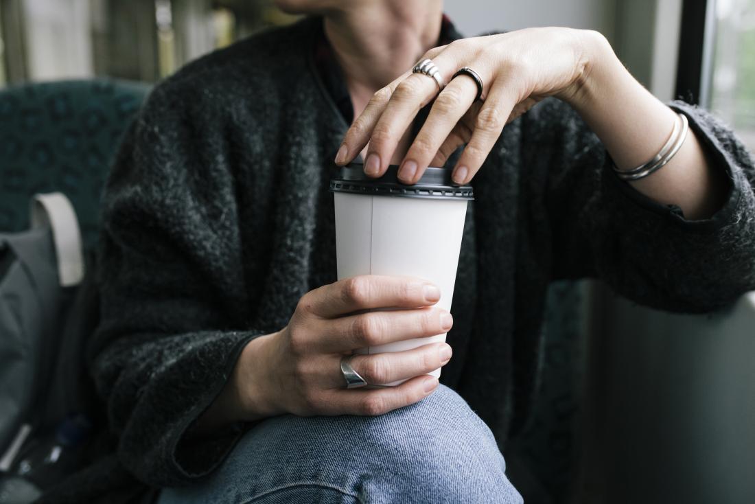 Woman experiencing caffeine withdrawal holding takeaway cup of coffee on public transport
