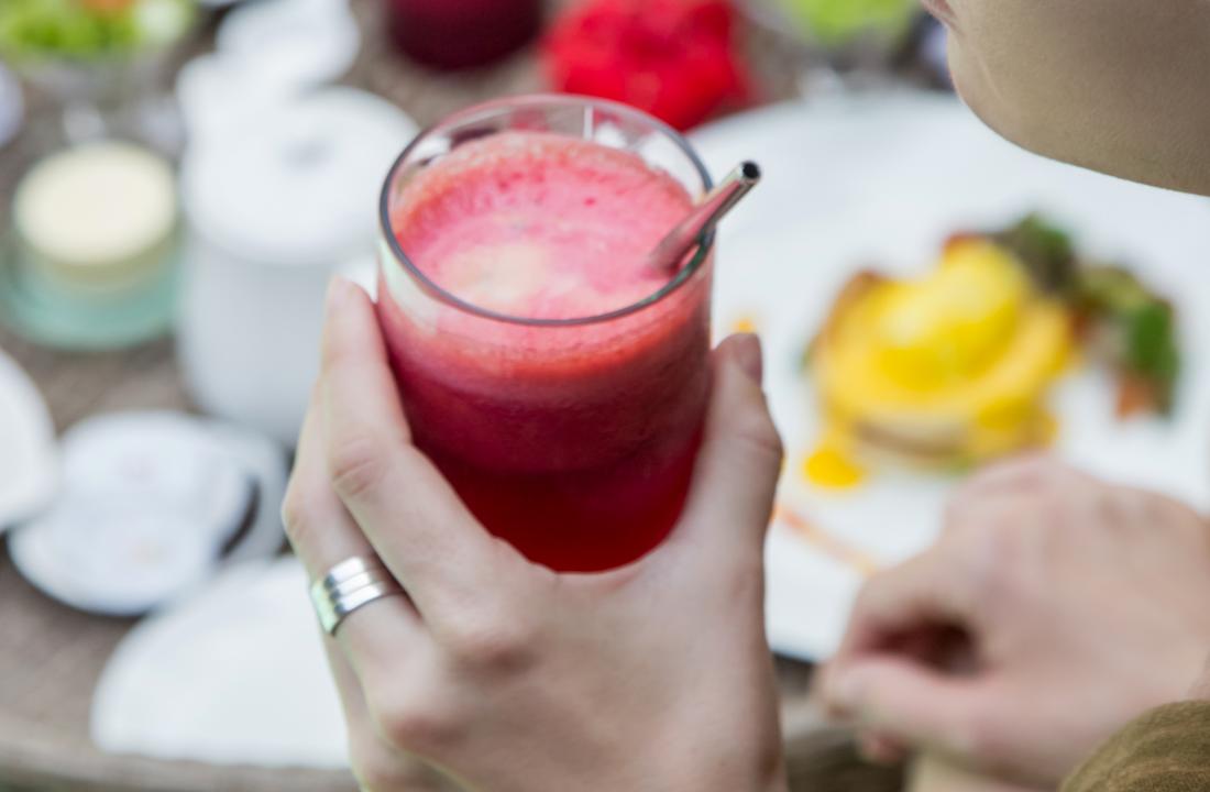 person drinking smoothie or juice made of beetroot-or pomegranate at breakfast table.