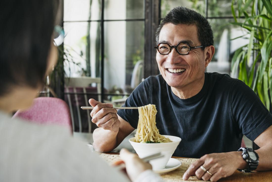 Man eating noodles in restaurant smiling and happy preventing type 2 diabetes