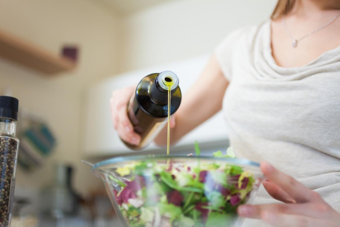 Woman pouring olive oil onto salad