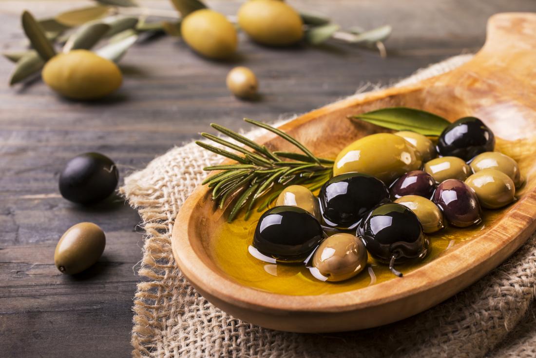 Different types of olives in oil in wooden bowl