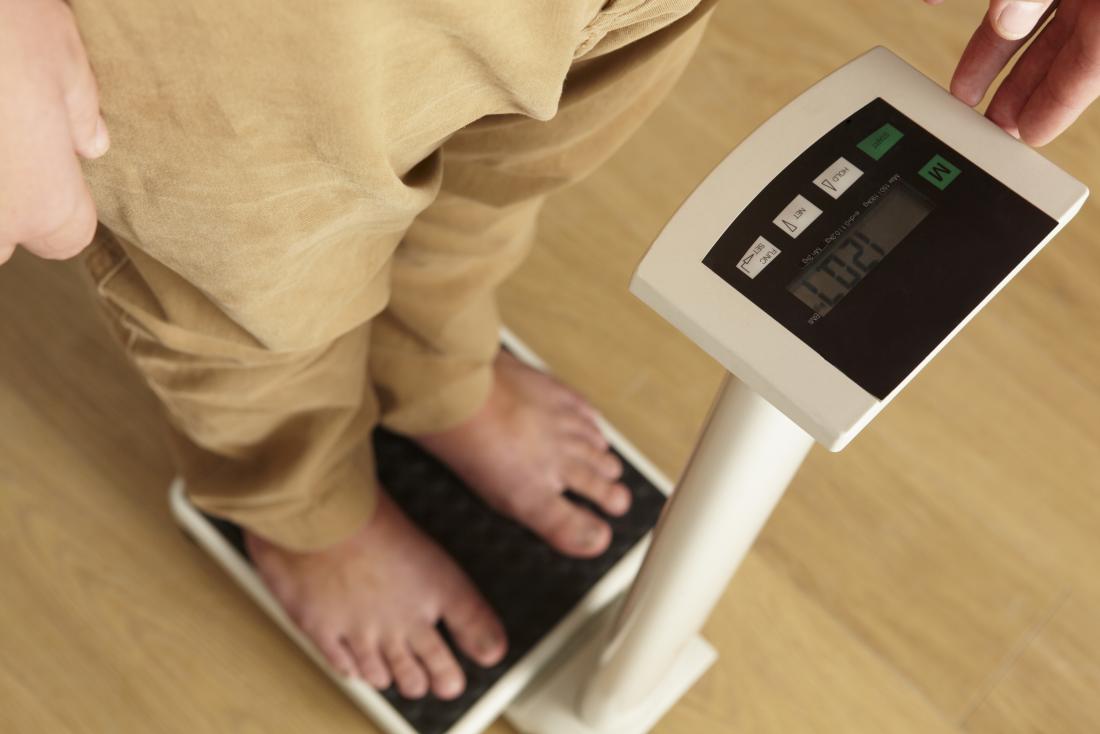 Man experiencing unexplained weight loss alongside heartburn and nausea stands on scales.