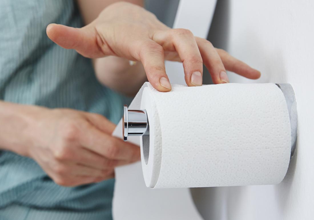 Woman experiencing blood in urine pulling toilet roll
