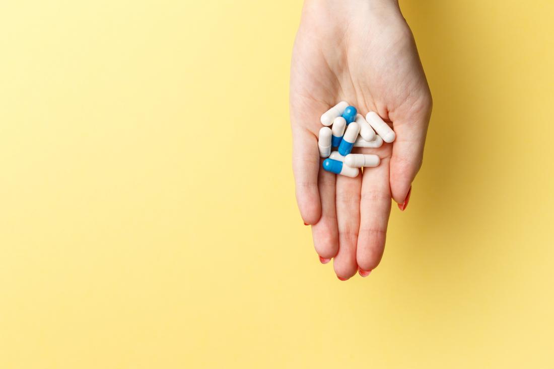 woman's palm holding white and blue pills against yellow background