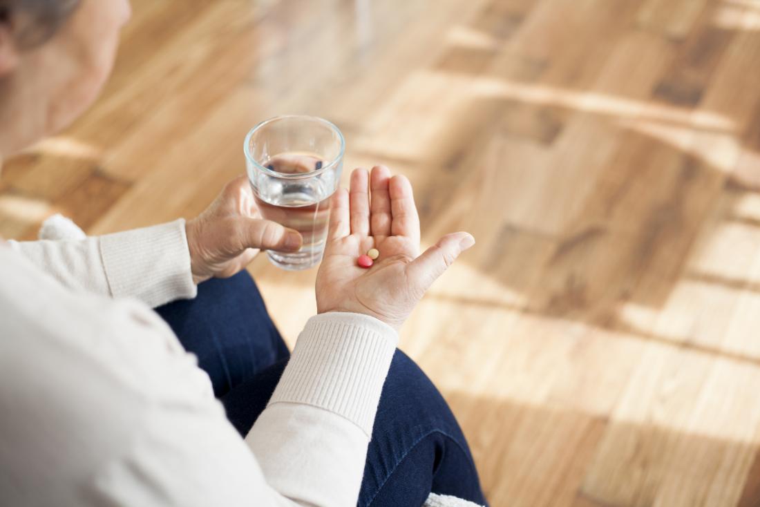 senior holding pills in one hand and a glass of water in the other