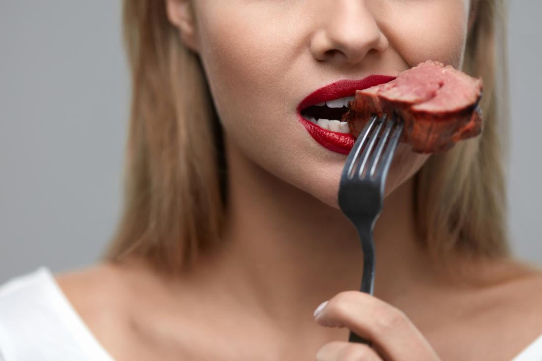 close up of woman's mouth eating red meat