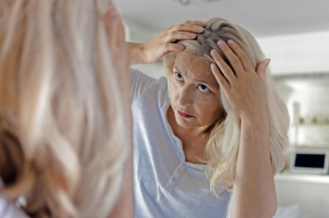 a woman inspecting her hair and wondering if a lack of ferritin is causing hair loss.