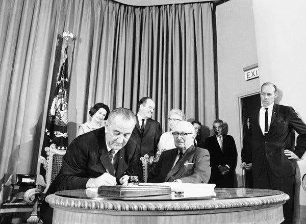 Lyndon B. Johnson in 1965, signing into law the bill that created Medicare and Medicaid. Looking on is Harry Truman, who sought to introduce universal health care during his presidency.