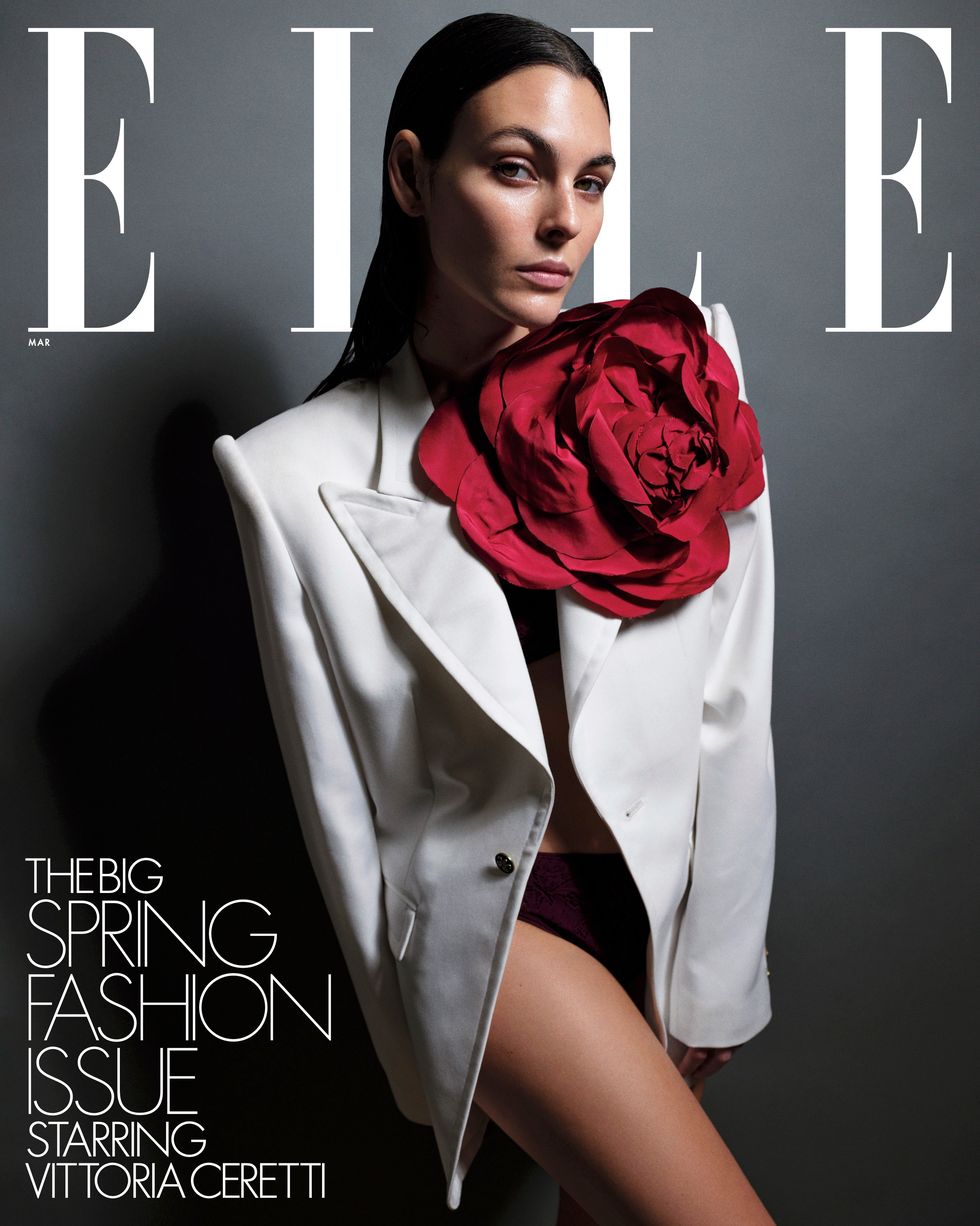 a brunette woman wearing a white blazer and red rosette