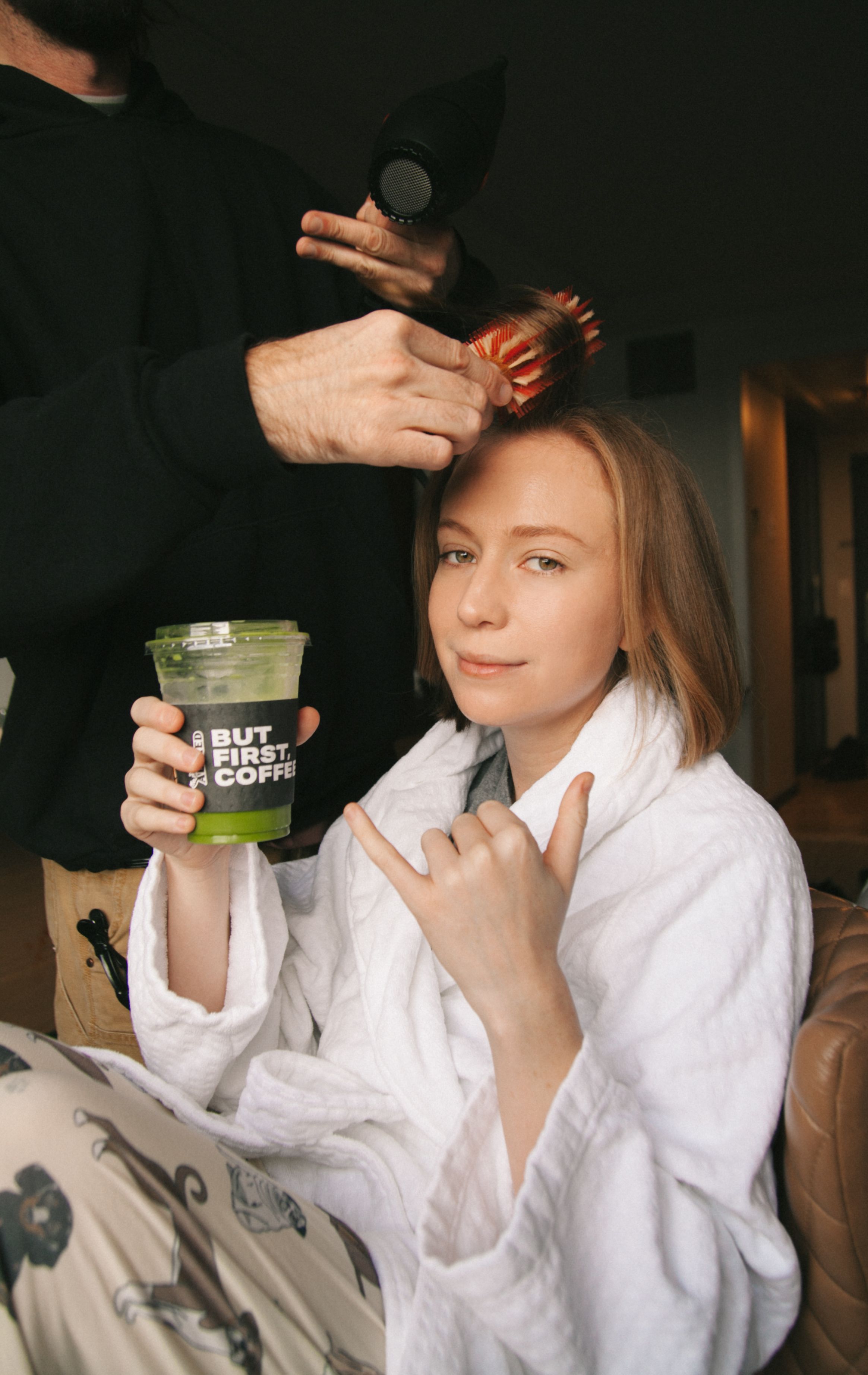 hannah einbinder holding a green juice and making a rock on sign at the camera