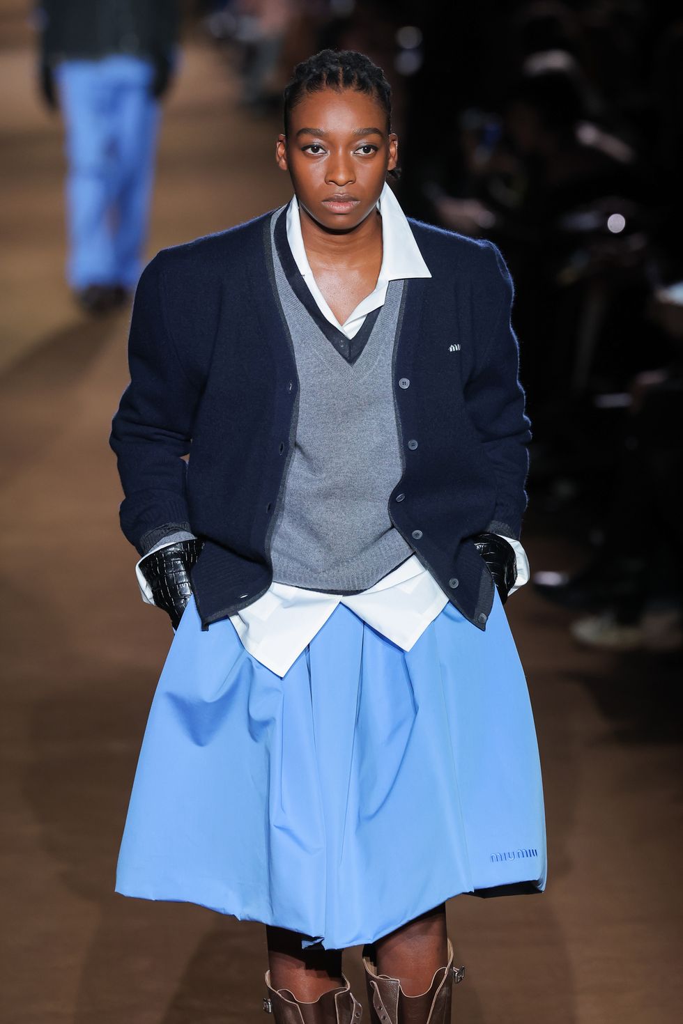 a model walks the runway in a black blazer and light blue skirt