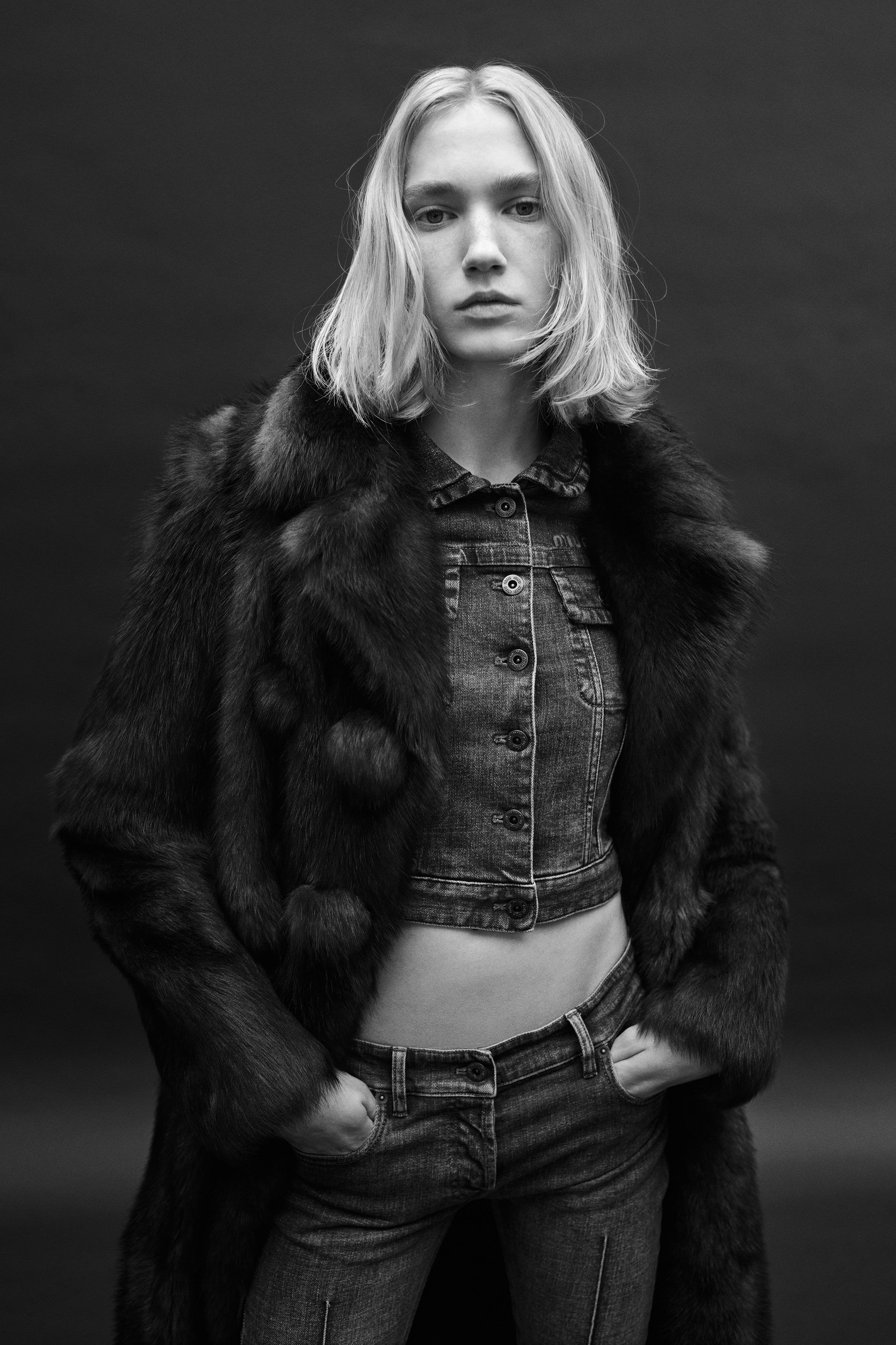 a woman with a blond bob wearing a crop top, jeans and a jacket