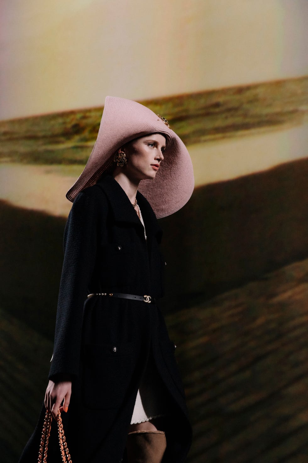 a model in an oversized pink hat walking the runway