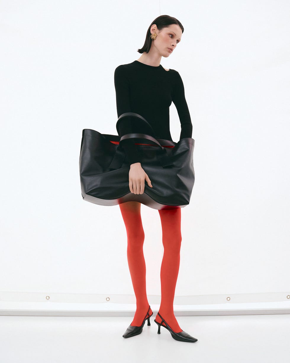 a woman in a black dress and red tights holding an oversized black bag