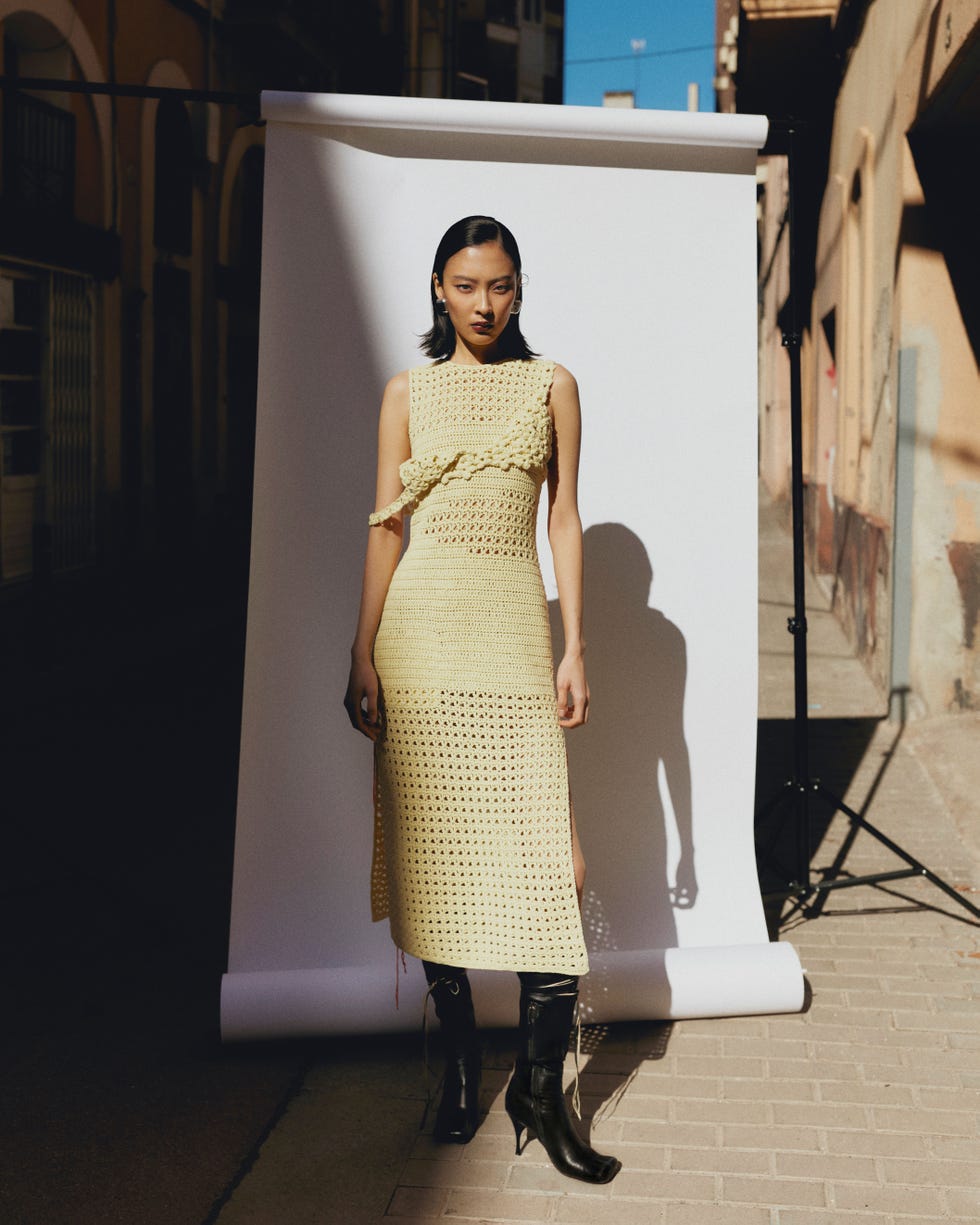 a woman in a yellow crochet dress standing in front of a white seamless backdrop