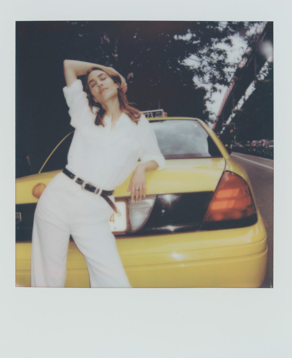 a woman in a white shirt and pants leaning on a yellow taxi cab