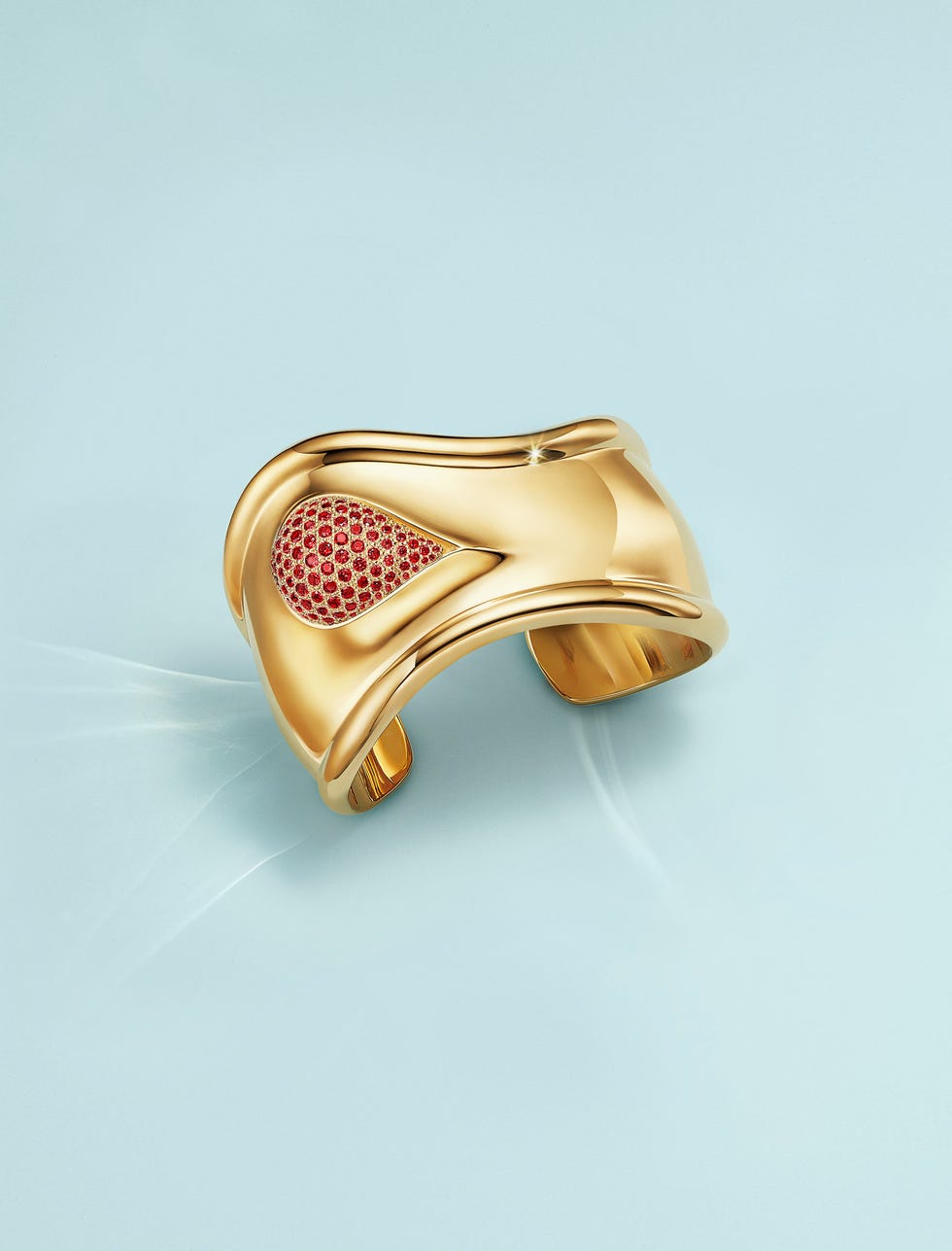 a gold and ruby cuff against a pastel blue background