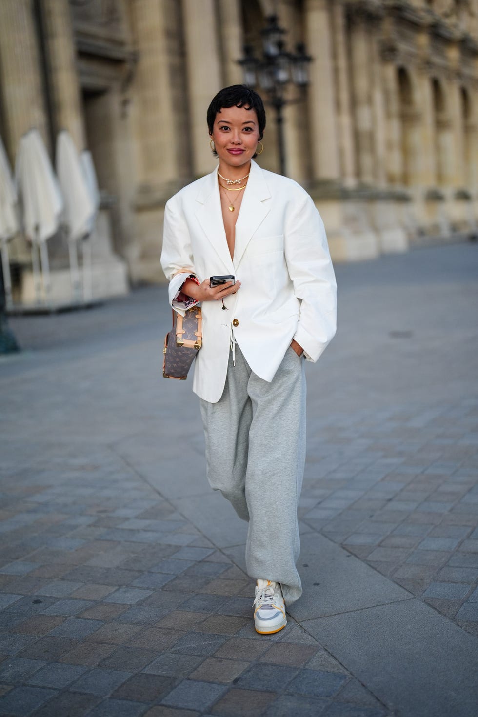 a fashionable individual is strolling outdoors, wearing a loose white blazer over a top, paired with gray sweatpants